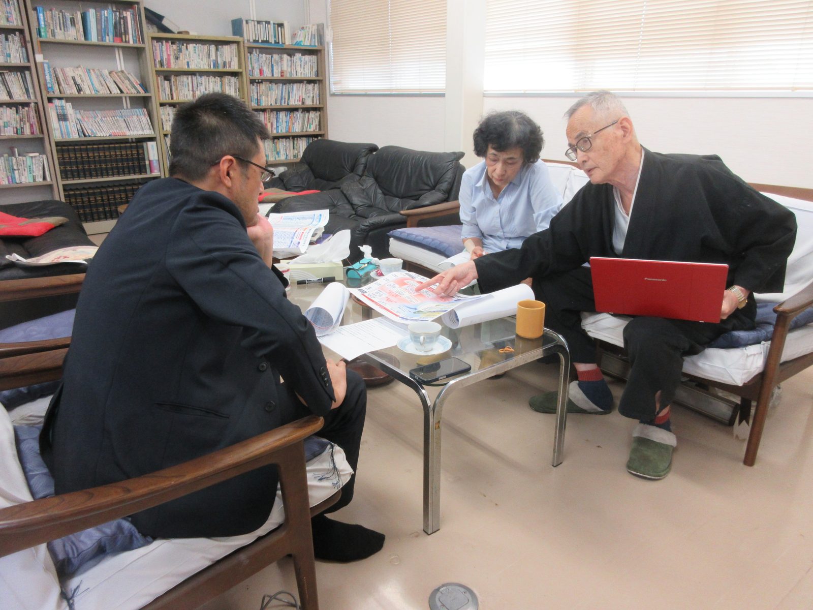 家族根っ子会議。低い机を囲んで、藤井薫が資料を指さし、家族が見ている。